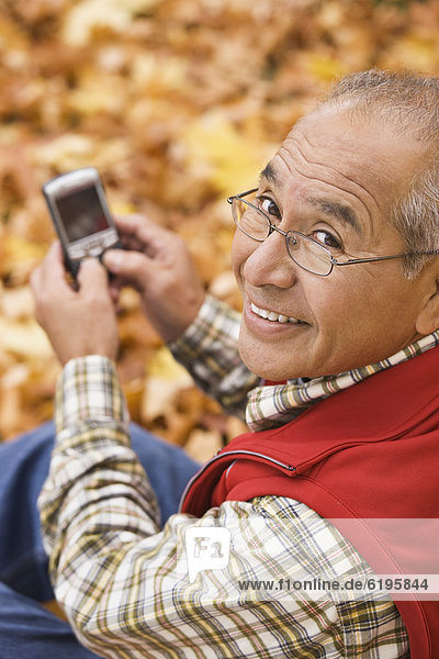 Hispanic man using cell phone outdoors in autumn