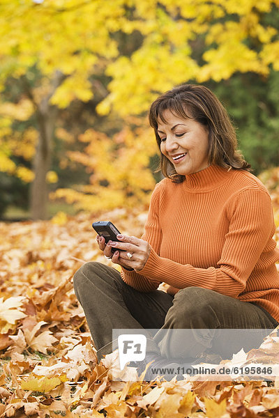 Hispanic woman using cell phone outdoors in autumn