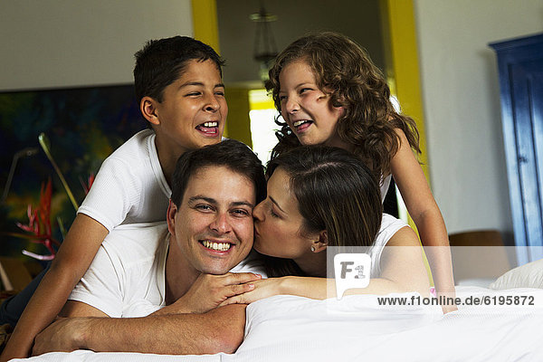 Smiling Hispanic family laying on bed together