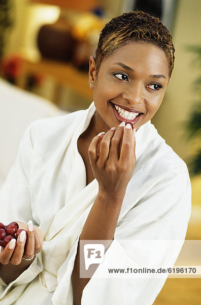 African woman in bathrobe eating grape