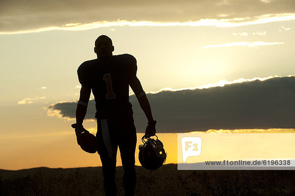 Silhouette of Black football player carrying helmet and football