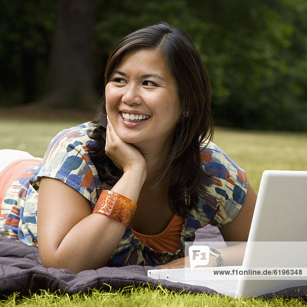Asian woman laying in park with laptop