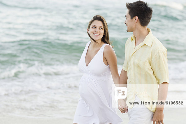 Husband holding hands with pregnant wife on beach