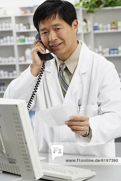 Asian male pharmacist talking on telephone