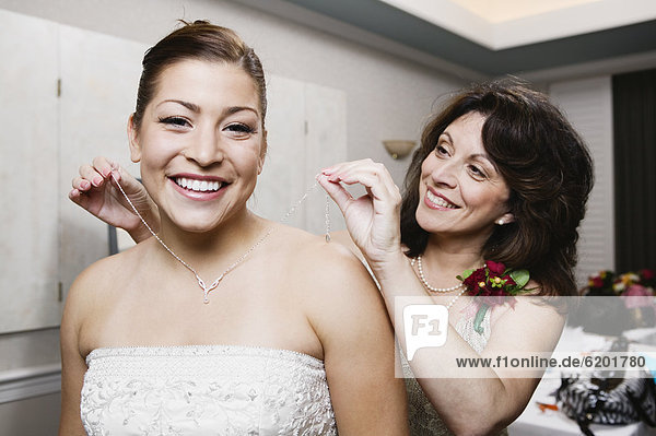Bride's mother putting necklace on daughter