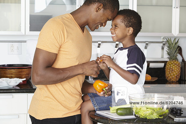 African American father and son making salad in kitchen