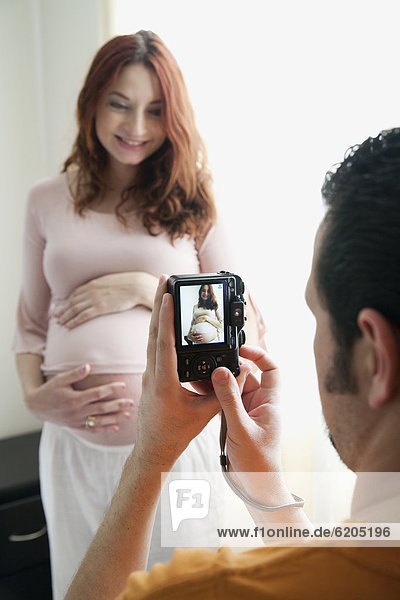 Hispanic man taking photograph of pregnant wife