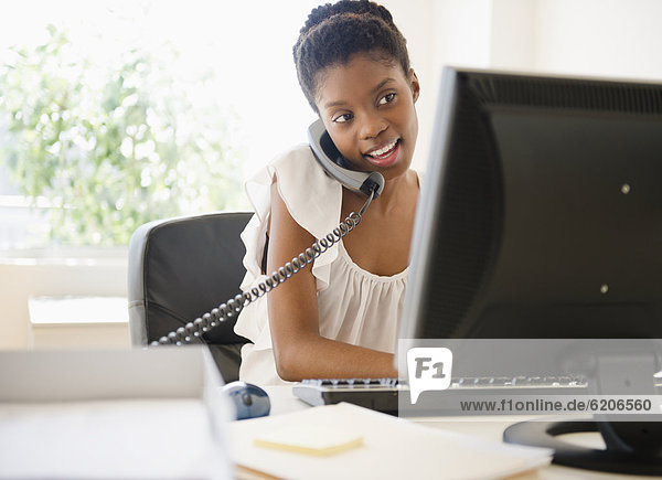 Black businesswoman talking on phone and using laptop