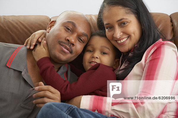 Mixed race boy snuggling on couch with parents