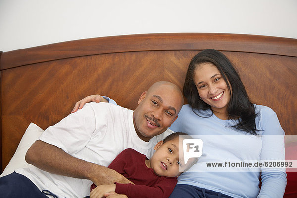 Mixed race boy lounging in bed with parents