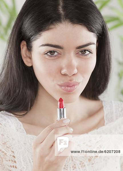 Hispanic woman applying lipstick mouth