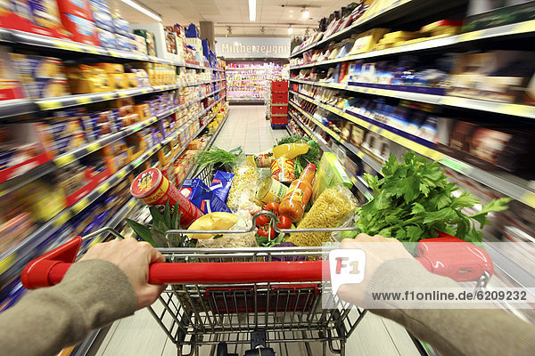 Full shopping trolley being pushed down the aisle  food hall  supermarket  Germany  Europe
