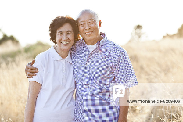 Smiling senior Chinese couple standing in field