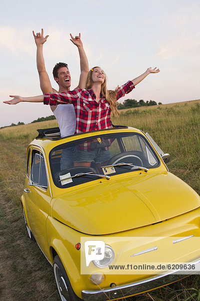 Caucasian couple standing in car sun roof in field