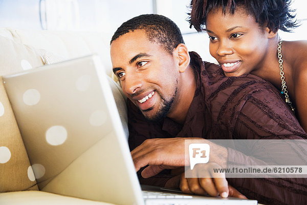 African couple using laptop on sofa