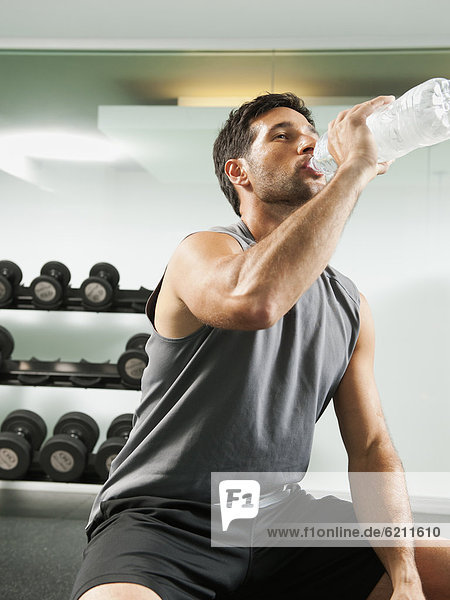 Mixed race man drinking water in gym