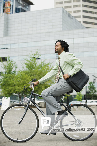 Mixed race businessman riding bicycle in city