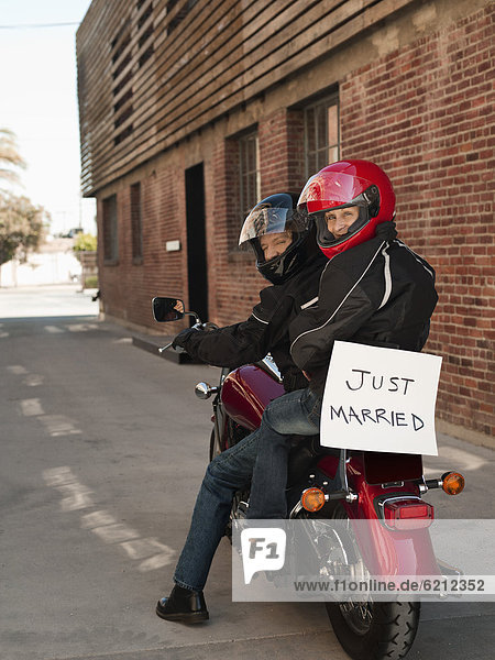 Caucasian couple riding on motorcycle with Just Married sign