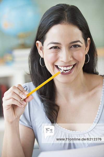 Smiling Hispanic woman biting pencil eraser