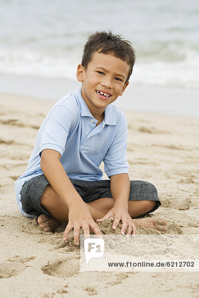 Mixed race boy playing with sand on beach