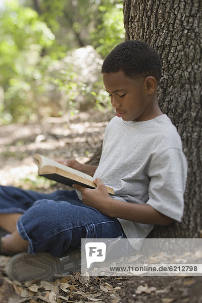 African boy reading book against tree