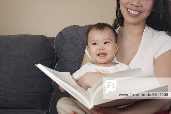 Chinese mother and baby reading book on sofa