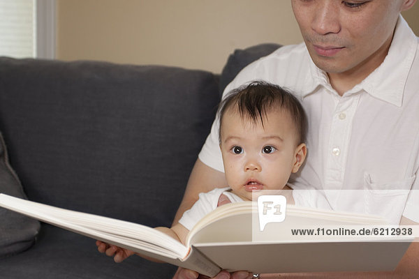 Chinese father and baby reading book on sofa