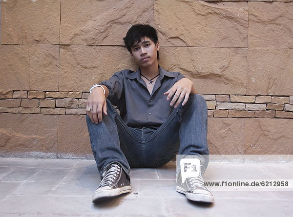 Asian man sitting against wall
