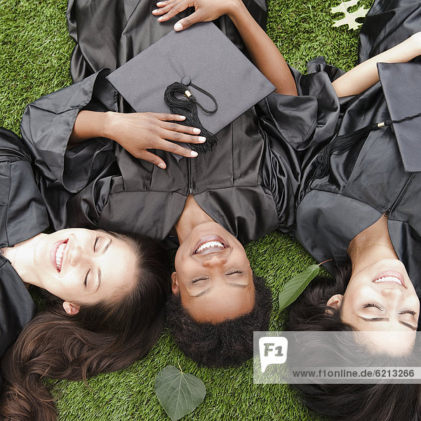 Friends in caps and gowns laying in grass
