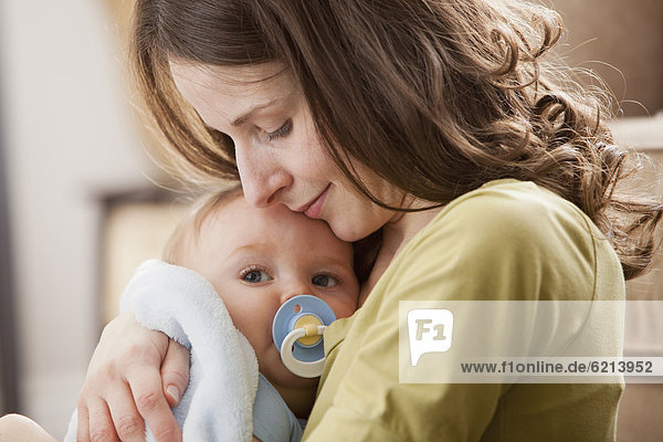 Caucasian baby boy with pacifier in mother's arms
