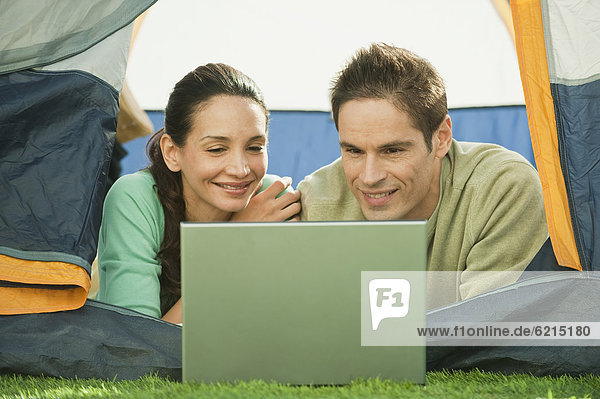 Hispanic couple using laptop in tent