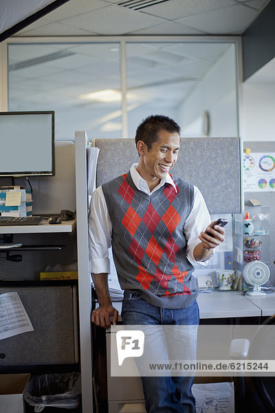 Mixed race businessman using cell phone in office cubicle