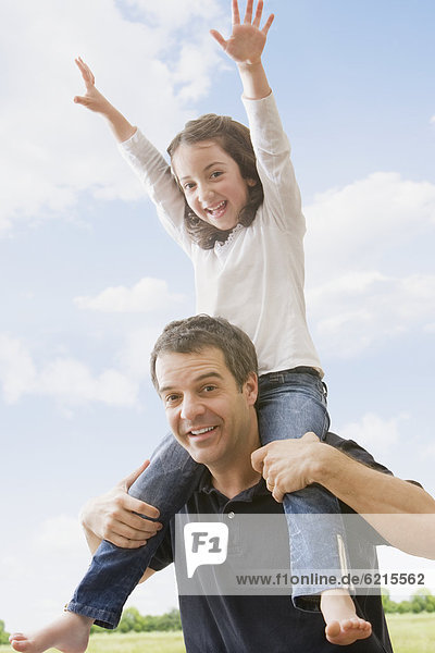 Hispanic father carrying daughter on shoulders
