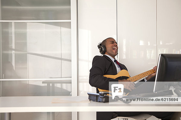 Black businessman playing guitar at desk