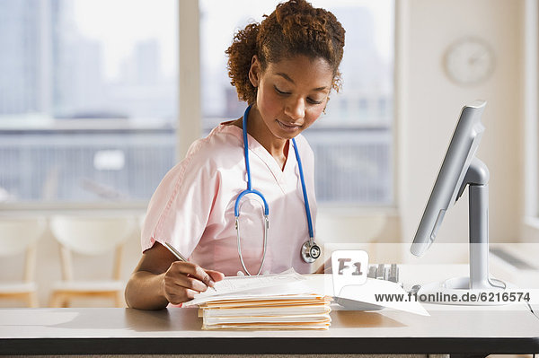 Mixed race nurse working on medical charts at computer