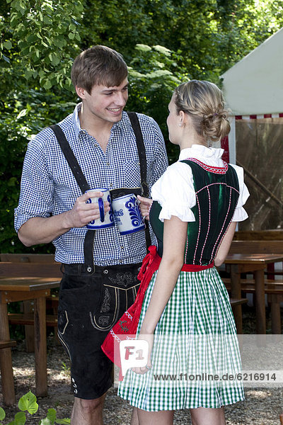 Junges Paar in Dirndl und Lederhose unterhält sich im Biergarten  bei Pettstatt  Oberfranken  Bayern  Deutschland  Europa