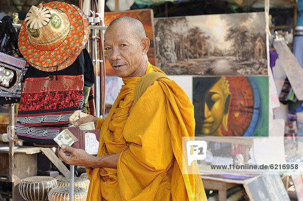 Buddhist monk buying statues of saints from a souvenir shop on the grounds of Angkor Wat  Cambodia  South East Asia