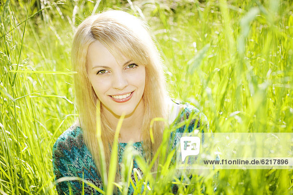 Lächelnde junge Frau sitzt im hohen Gras