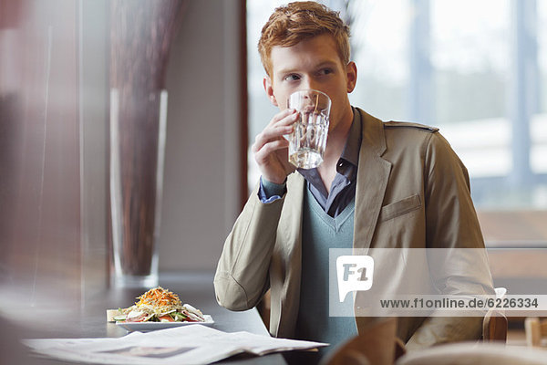 Mann sitzt in einem Restaurant und trinkt Wasser.