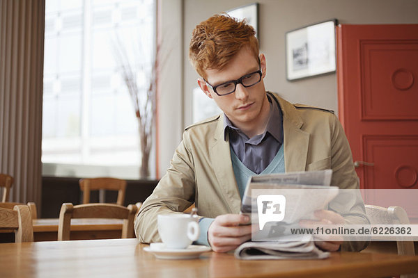 Ein Mann  der in einem Restaurant sitzt und eine Zeitung liest.