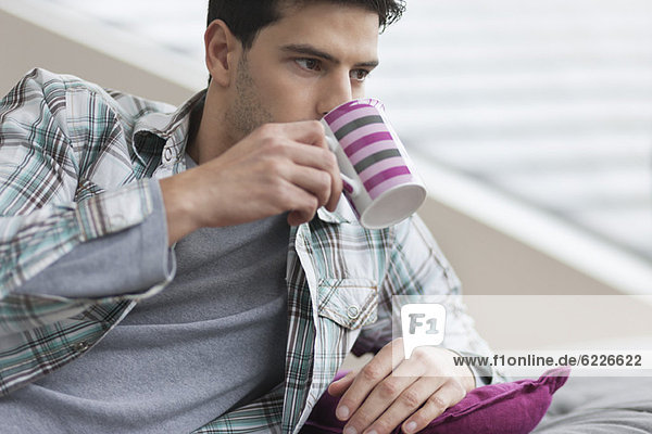Mann auf der Couch liegend und Kaffee trinkend