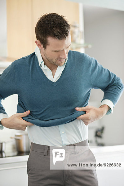 Man putting on sweater in the kitchen