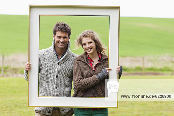 Porträt eines Paares  das einen Rahmen in einem Feld hält.