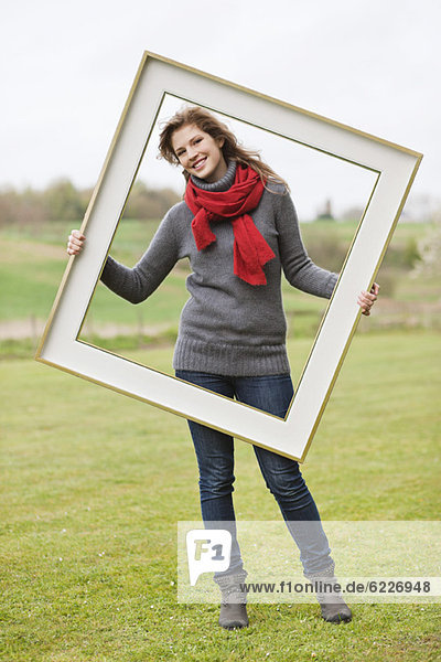 Portrait of a woman standing with a frame in a park