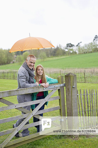 Mann steht mit seiner Tochter auf einem Bauernhof mit Regenschirm