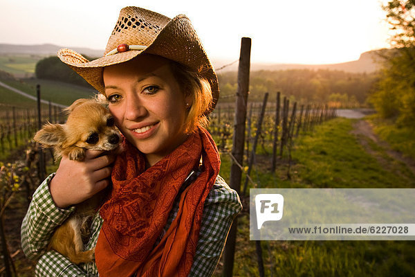 Lächelnde junge Frau mit Hut hält einen Hund  Portrait