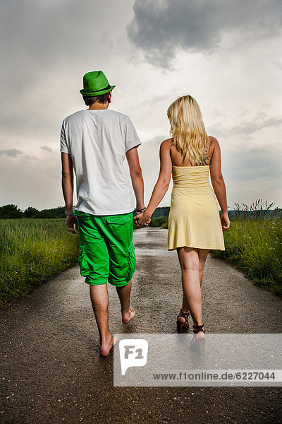 Junges Paar geht Hand in Hand in ländlicher Umgebung