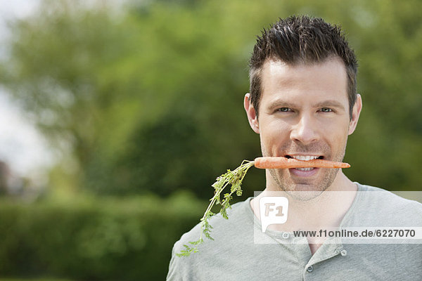 Mann hält eine Karotte im Mund.