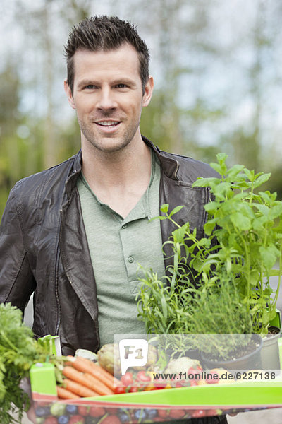 Mann hält ein Tablett mit rohem Gemüse.