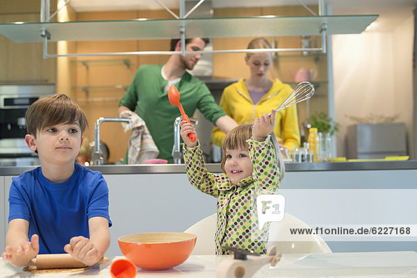 Kinder kochen in der Küche mit ihren Eltern im Hintergrund